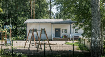Daghemmet Lilla-Lotta med vit träfasad syns i bakgrunden. Framför daghemmet finns en lekplats med en gunga, sandlåda och en klätterställning.
