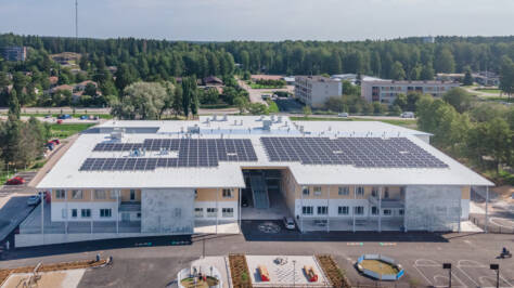 Flygbild på bilndingscampuset Sjundeå hjärta. På byggnadens tak finns solpaneler, skolgården är stor med olika lekmöjligheter.
