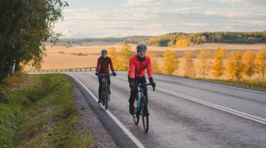 Nainen ja mies pyöräilevät Lappersintiellä Gårdskullan koivukujan edustalla syksyisessä maisemassa.