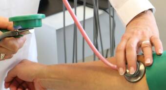 Ojennettu käsivarsi, josta mitataan verenpainetta ja johon toisen henkilön käsi painaa stetoskooppia.