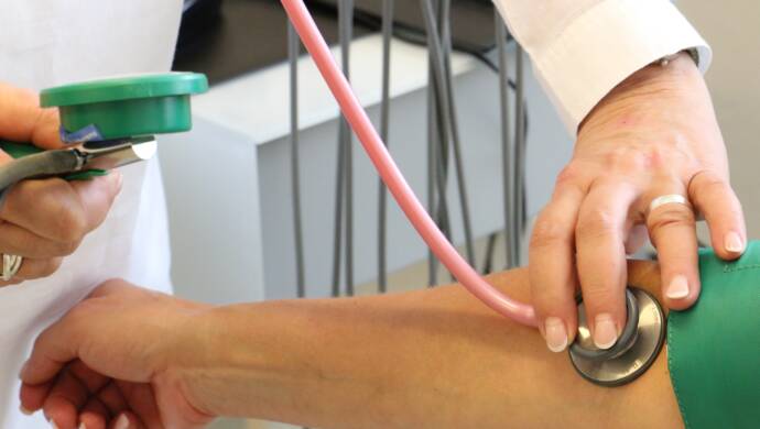 Ojennettu käsivarsi, josta mitataan verenpainetta ja johon toisen henkilön käsi painaa stetoskooppia.