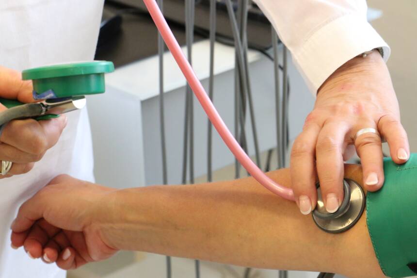 Blodtryck mäts på en utsträckt arm och en annan persons hand trycker ett stetoskop mot armbågen.